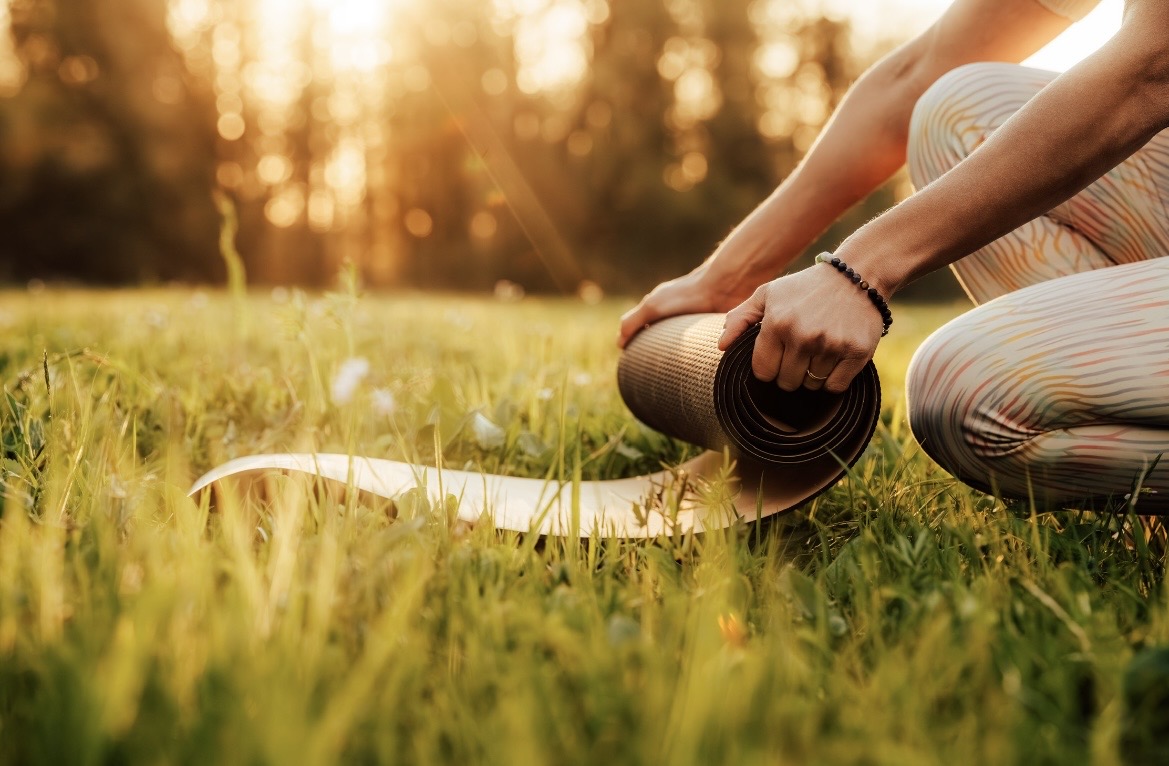 Hände rollen eine Korkmatte im sonnigen Gras aus